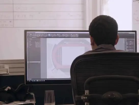 Civil Engineer sitting at his desk looking at his computer with a 3D drawing of a sportsfield on it