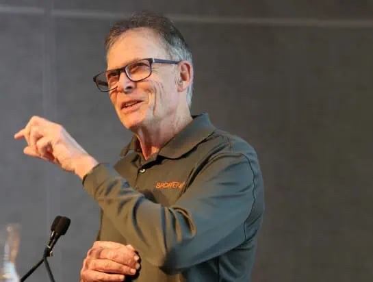 Man in his sixties on a podium talking to microphone during a conference