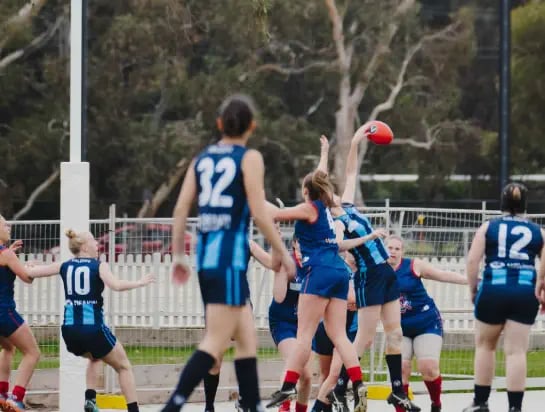 Group of girls wearing team colours playing AFL on a sportsfield
