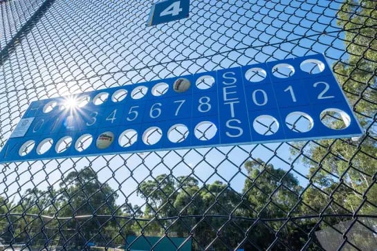 Blue tennis score board hang on an outdoor tennis court fence