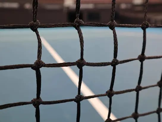 Close up of a tennis net on an indoor tennis court with a blue acrylic surface