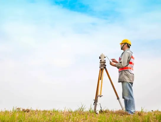 Worker with construction gear standing in front of a measuring tool on a natural turf sportsfield