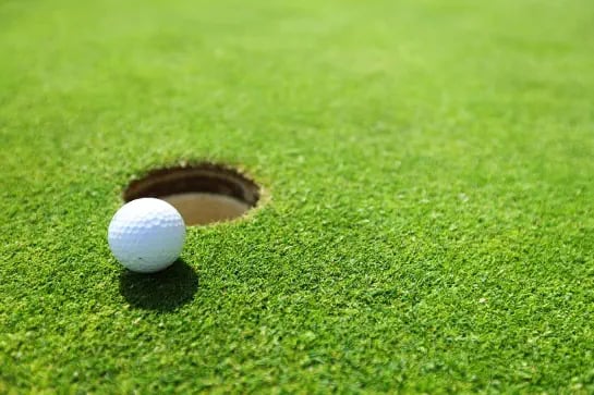 Golf ball next to a golf hole on a green