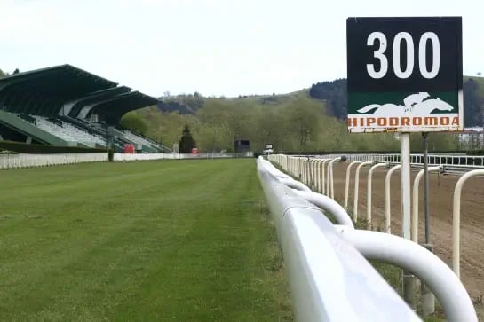 Horse racing track with white barrier on right side and grandstand on left side