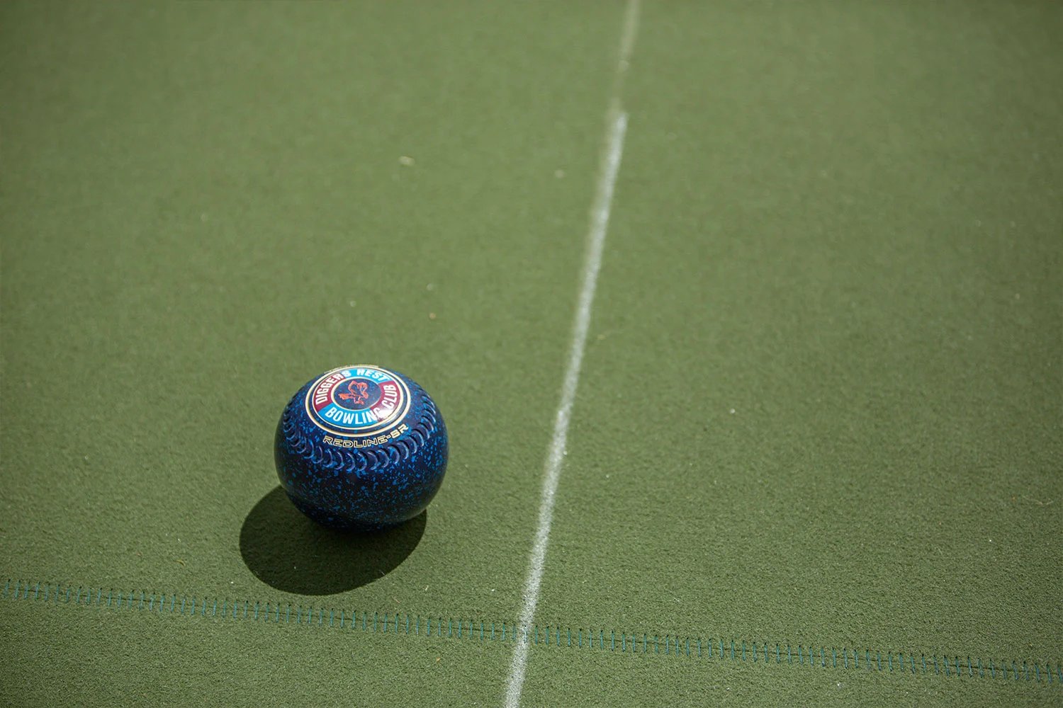 Close up of a lawn bowl on a synthetic turf surface with white line marking