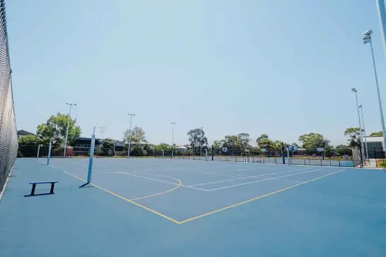 Panoramic view of an outdoor netball court with blue surface and yellow line marking