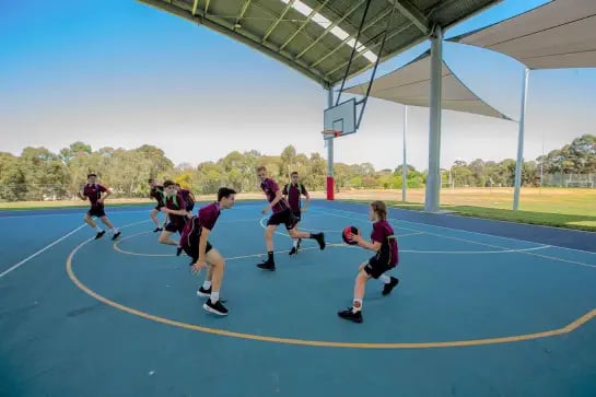 Students playing netball on an outdoor blue basketball surface
