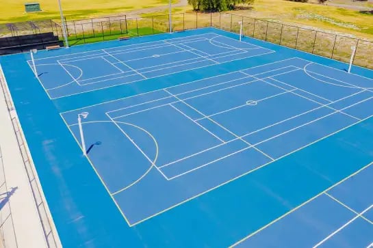 Aerial view of an outdoor blue netball surface surrounded by a park