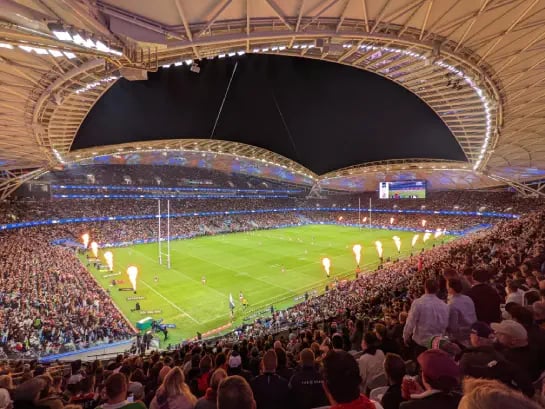 Panoramic view inside the Sydney Football Stadium at night with rugby players on the playing field and fans in grandstands