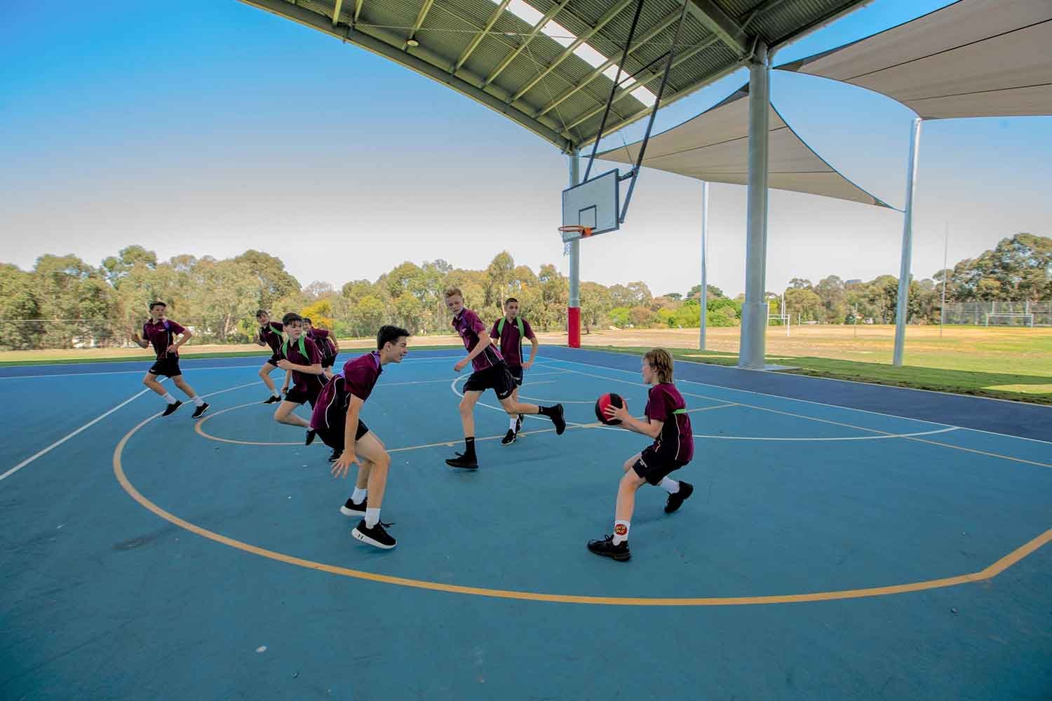 Students playing basketball on a outdoor acrylic blue surface sports field 