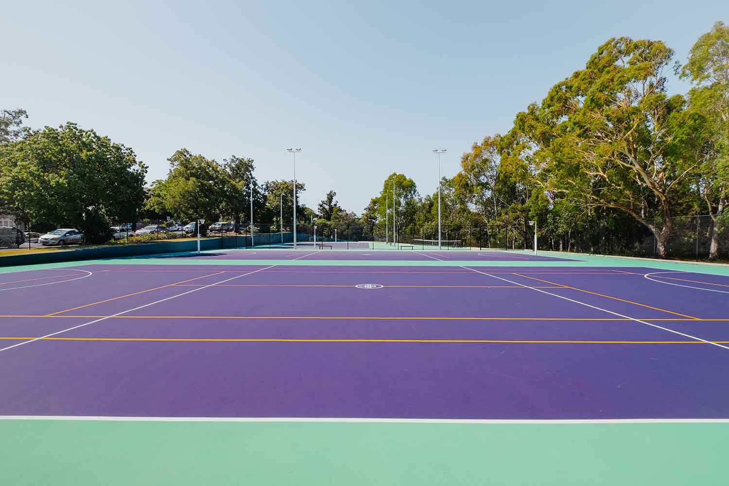 Outdoor green and purple acrylic surface sports fields with yellow and white lin markings, surrounded by trees