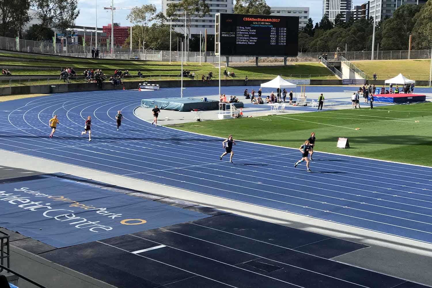 Aerial view of people running on blue outdoor athletic tracks with white line markings