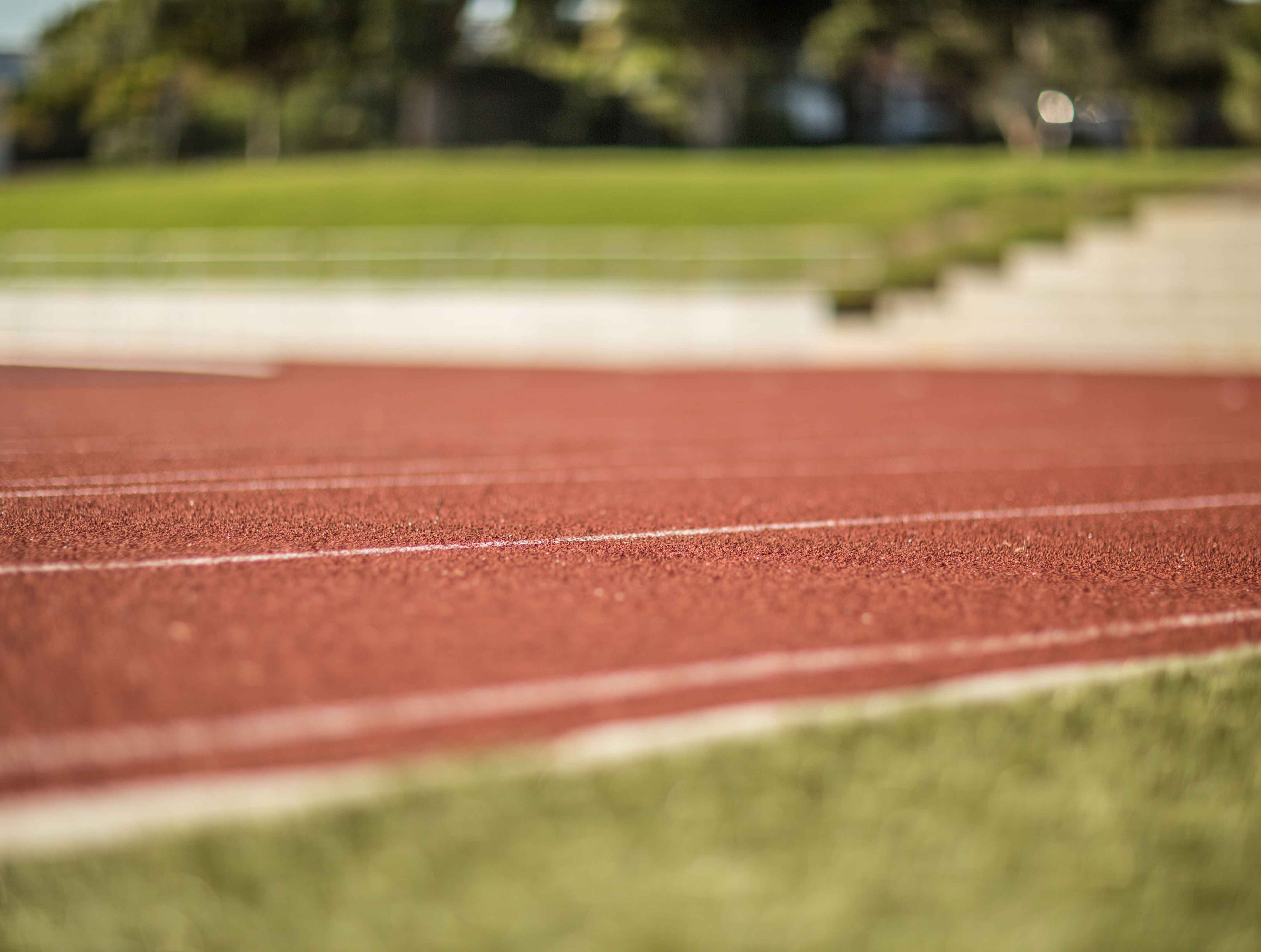 Close up of the red surface of an outdoor athletic track with blurry background