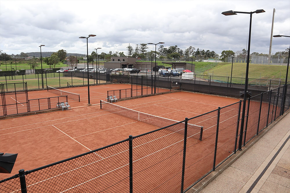 Aerial view of multiple outdoor red porous tennis courts surface with white line markings and black fences