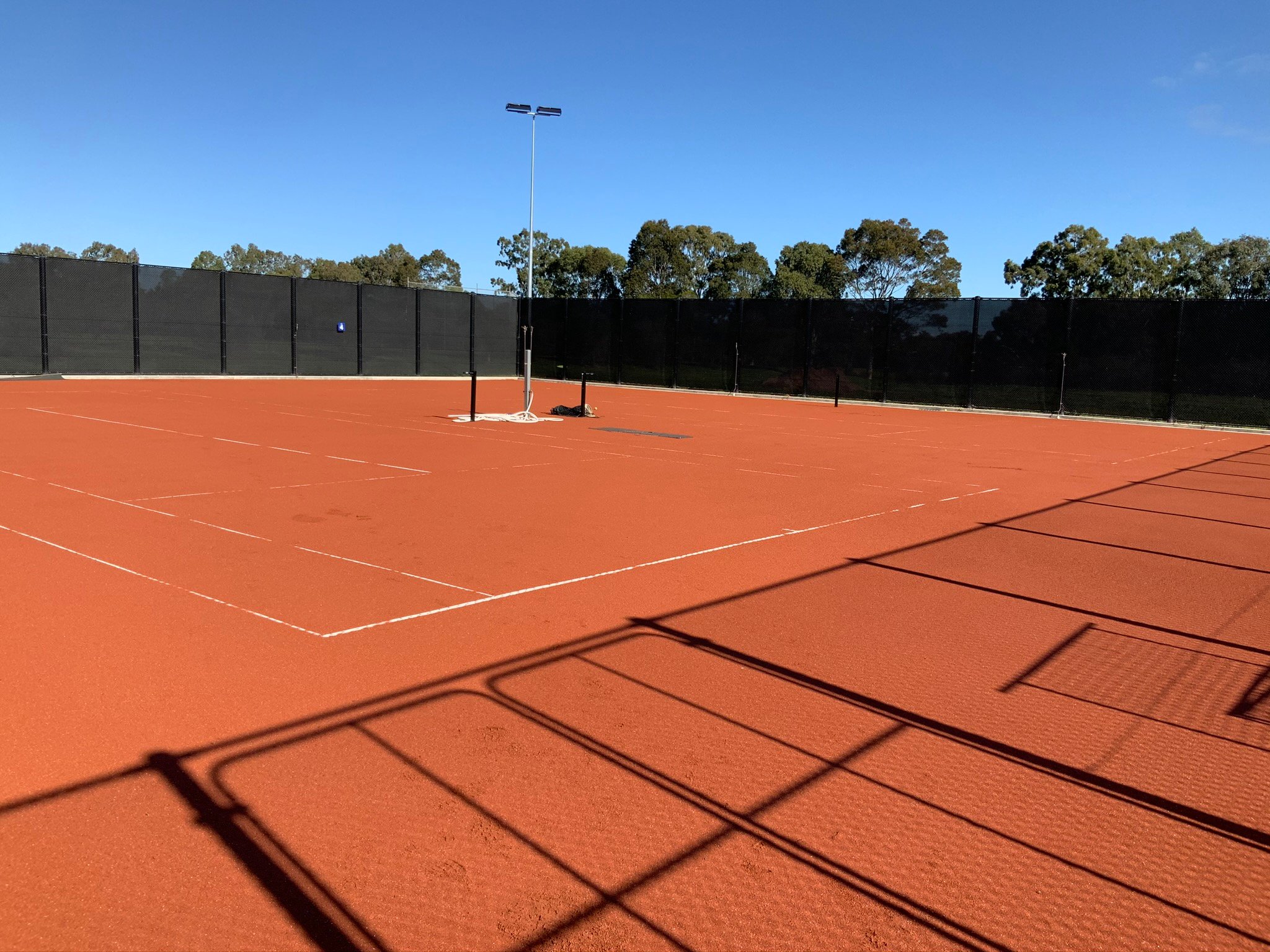 Panoramic view of an outdoor red porous tennis court surface with white line markings