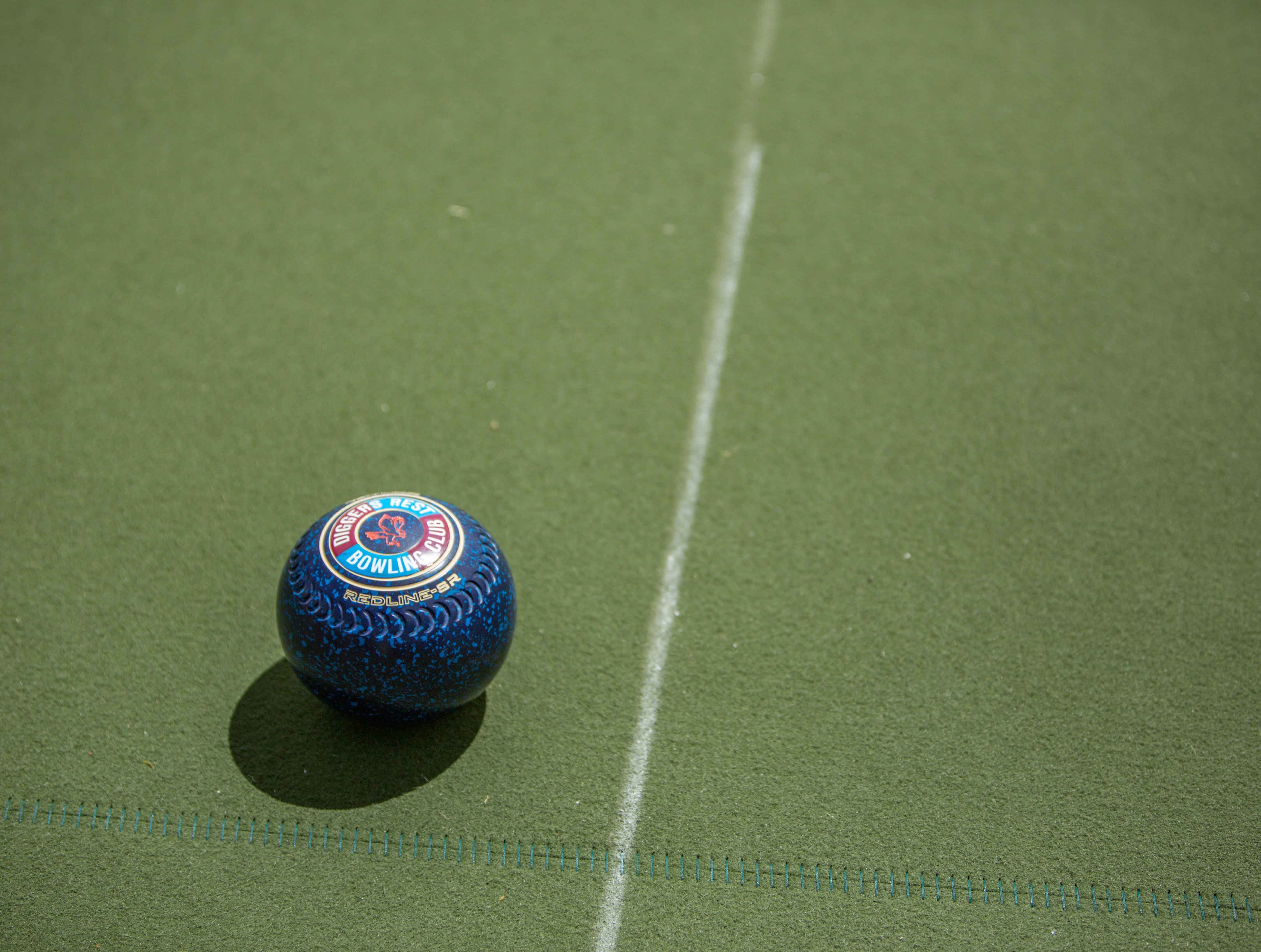 Close up of blue lawn bowl on an outdoor synthetic turf surface with a white line marking