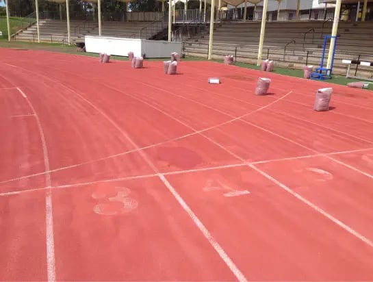 Close up of a red athletic track being constructed with line markings in progress