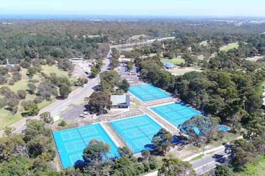 Aerial view of a set of blue tennis courts next to a park